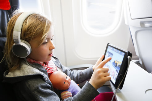 Kleines Mädchen sitzt in einem Flugzeug und schaut etwas auf einem digitalen Tablet an - FKF02331