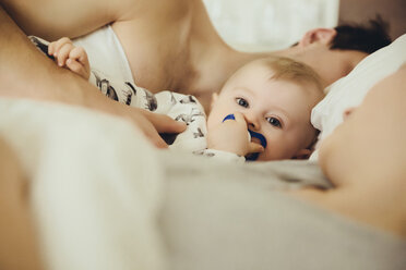Baby boy cuddling with parents in bed - MFF03644