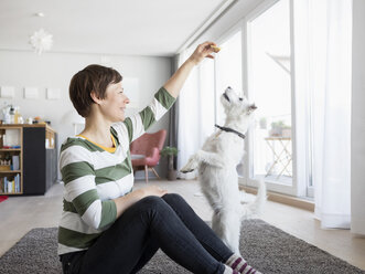 Frau sitzt mit ihrem Hund auf dem Boden im Wohnzimmer - RBF05670