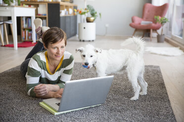 Frau liegt auf dem Boden in ihrer Wohnung und schaut auf einen Laptop - RBF05674