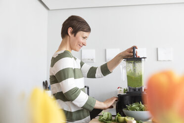Lächelnde Frau bei der Zubereitung eines grünen Smoothies in der Küche - RBF05679