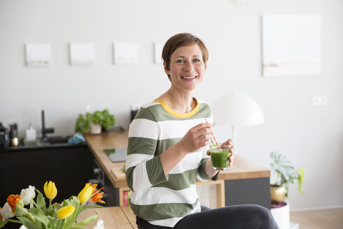 Porträt einer lächelnden Frau mit grünem Smoothie in der Küche - RBF05680