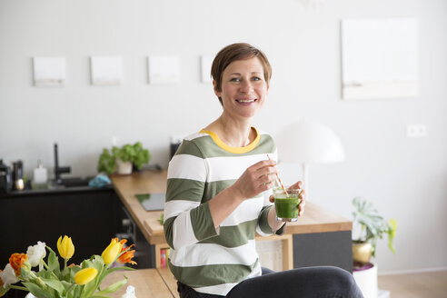 Portrait of smiling woman with green smoothie in the kitchen - RBF05680