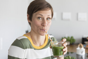 Porträt einer Frau, die in der Küche einen grünen Smoothie trinkt - RBF05682