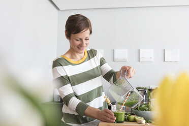 Lächelnde Frau gießt grünen Smoothie in ein Glas - RBF05684