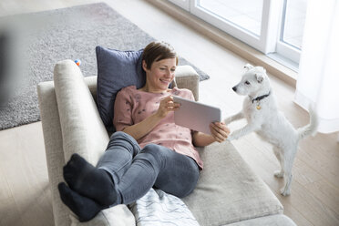 Porträt einer lächelnden Frau, die sich mit einem Tablet auf der Couch entspannt - RBF05690