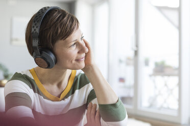 Lächelnde Frau, die zu Hause mit Kopfhörern Musik hört - RBF05699