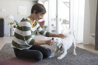 Lächelnde Frau, die zu Hause auf dem Boden sitzt und mit ihrem Hund spielt - RBF05704