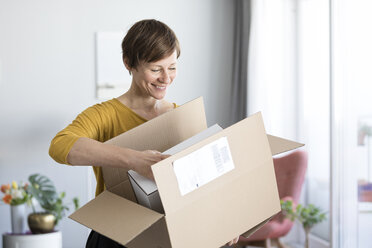 Lächelnde Frau beim Auspacken eines Pakets zu Hause - RBF05716