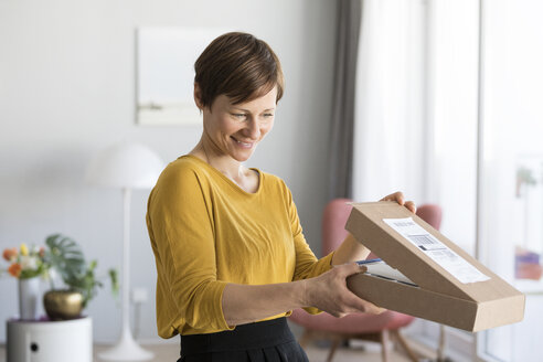 Smiling woman unpacking parcel at home - RBF05717