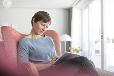Porträt einer Frau, die zu Hause auf einem Sessel sitzt und ein Tablet benutzt - RBF05720