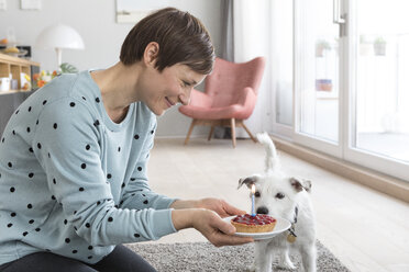 Lächelnde Frau präsentiert ihrem Hund eine Geburtstagstorte - RBF05727