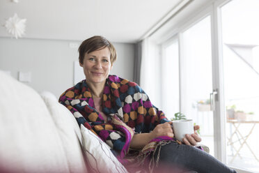 Portrait of smiling woman relaxing with cup of coffee on the couch - RBF05732