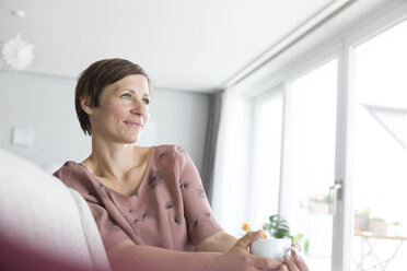 Portrait of smiling woman relaxing with cup of coffee at home - RBF05735