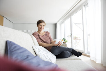Portrait of smiling woman relaxing with cup of coffee on the couch - RBF05736