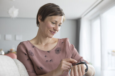 Portrait of smiling woman using smartwatch at home - RBF05737