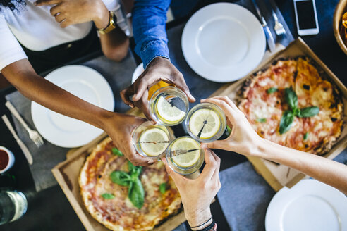 Eine Gruppe von Freunden isst zu Hause Pizza und stößt mit einem Glas Wasser an - GIOF02740