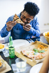 Young man enjoying slice of pizza at dining table - GIOF02742