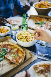 Hand greift nach Pommes frites auf dem Tisch - GIOF02746