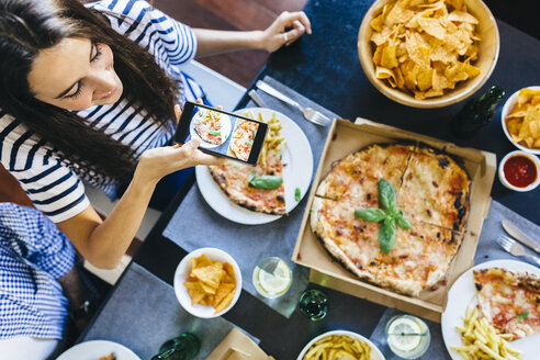 Frau nimmt Handy-Foto von Pizza auf dem Tisch - GIOF02753