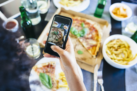 Hand taking cell phone picture of pizza on table stock photo