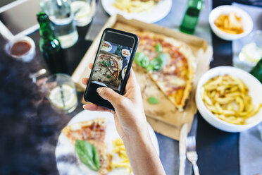 Hand nimmt Handy-Foto von Pizza auf dem Tisch - GIOF02754