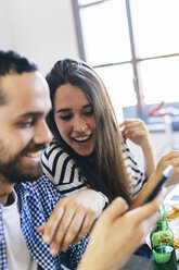 Couple looking at cell phone at dining table - GIOF02759