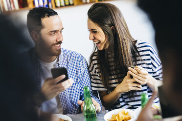 Happy couple sharing cell phone at dining table - GIOF02765