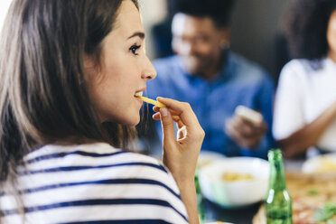 Woman eating French fry with friends in background - GIOF02767