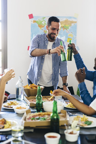 Eine Gruppe von Freunden stößt am Esstisch mit Bierflaschen an, lizenzfreies Stockfoto