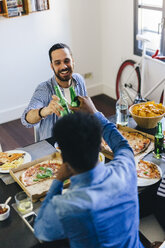 Friends clinking beer bottles at dining table - GIOF02772