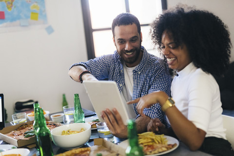 Glückliches Paar teilt sich ein Tablet am Esstisch, lizenzfreies Stockfoto