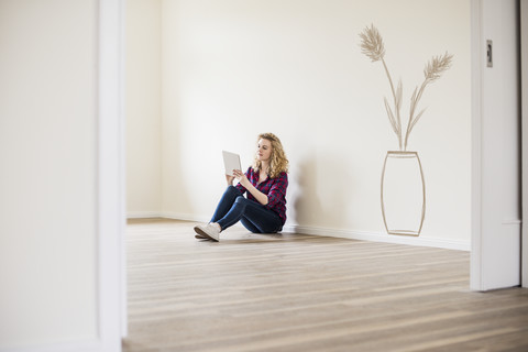 Junge Frau in neuer Wohnung sitzt auf dem Boden und benutzt ein Tablet, lizenzfreies Stockfoto