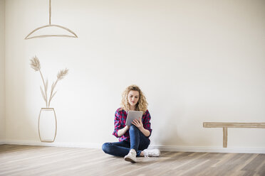 Young woman in new home sitting on floor using tablet - UUF10816