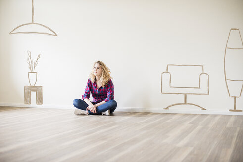 Young woman in new home sitting on floor thinking about interior design - UUF10817