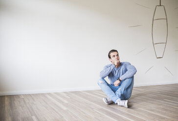 Young man in new home sitting on floor thinking about interior decoration - UUF10819