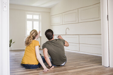 Young couple in new home sitting on floor thinking about interior design - UUF10822