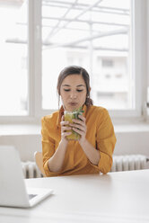 Young woman drinking tea at her desk - JOSF01088