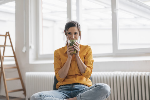 Junge Frau sitzt in ihrer neuen Wohnung und trinkt Tee, lizenzfreies Stockfoto