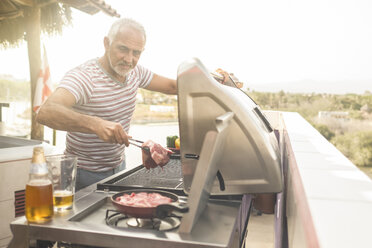 Älterer Mann grillt Steaks auf einem Gasgrill auf der Terrasse seines Penthouses - ABAF02158