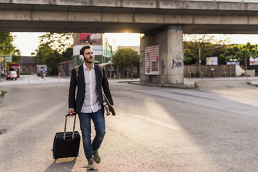 Young man on the move with skateboard, rolling suitcase and headphones - UUF10837