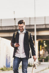 Smiling young man on the move checking cell phone - UUF10845