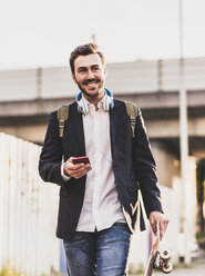 Smiling young man on the move holding cell phone - UUF10846