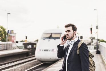 Junger Mann benutzt Handy auf dem Bahnsteig, als der Zug einfährt - UUF10852