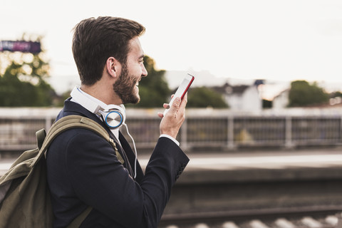 Lächelnder junger Mann mit Handy auf dem Bahnsteig, lizenzfreies Stockfoto