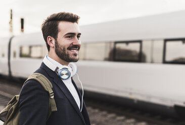 Lächelnder junger Mann auf dem Bahnsteig, als der Zug einfährt - UUF10854