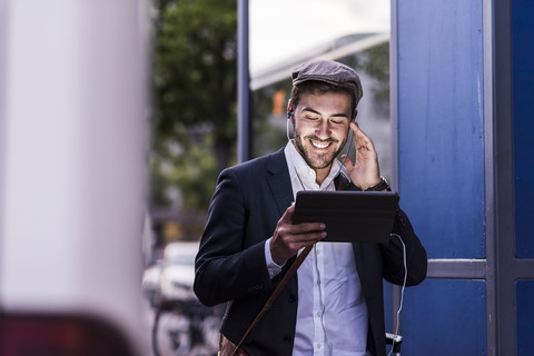 Lächelnder junger Mann in der Stadt mit Kopfhörern und Tablet, lizenzfreies Stockfoto