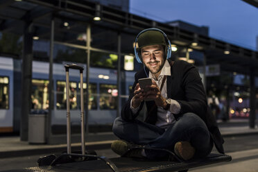 Junger Mann in der Stadt mit Kopfhörern und Mobiltelefon am Abend - UUF10865