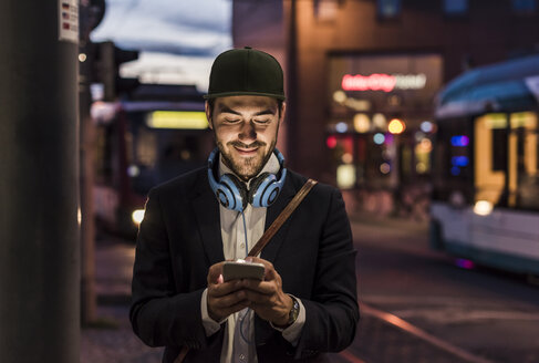 Junger Mann in der Stadt, der am Abend sein Handy überprüft - UUF10867