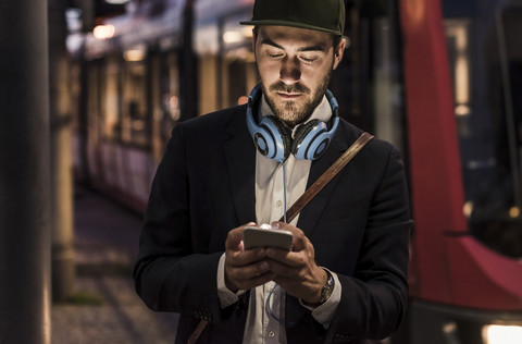 Junger Mann in der Stadt, der am Abend sein Handy überprüft, lizenzfreies Stockfoto